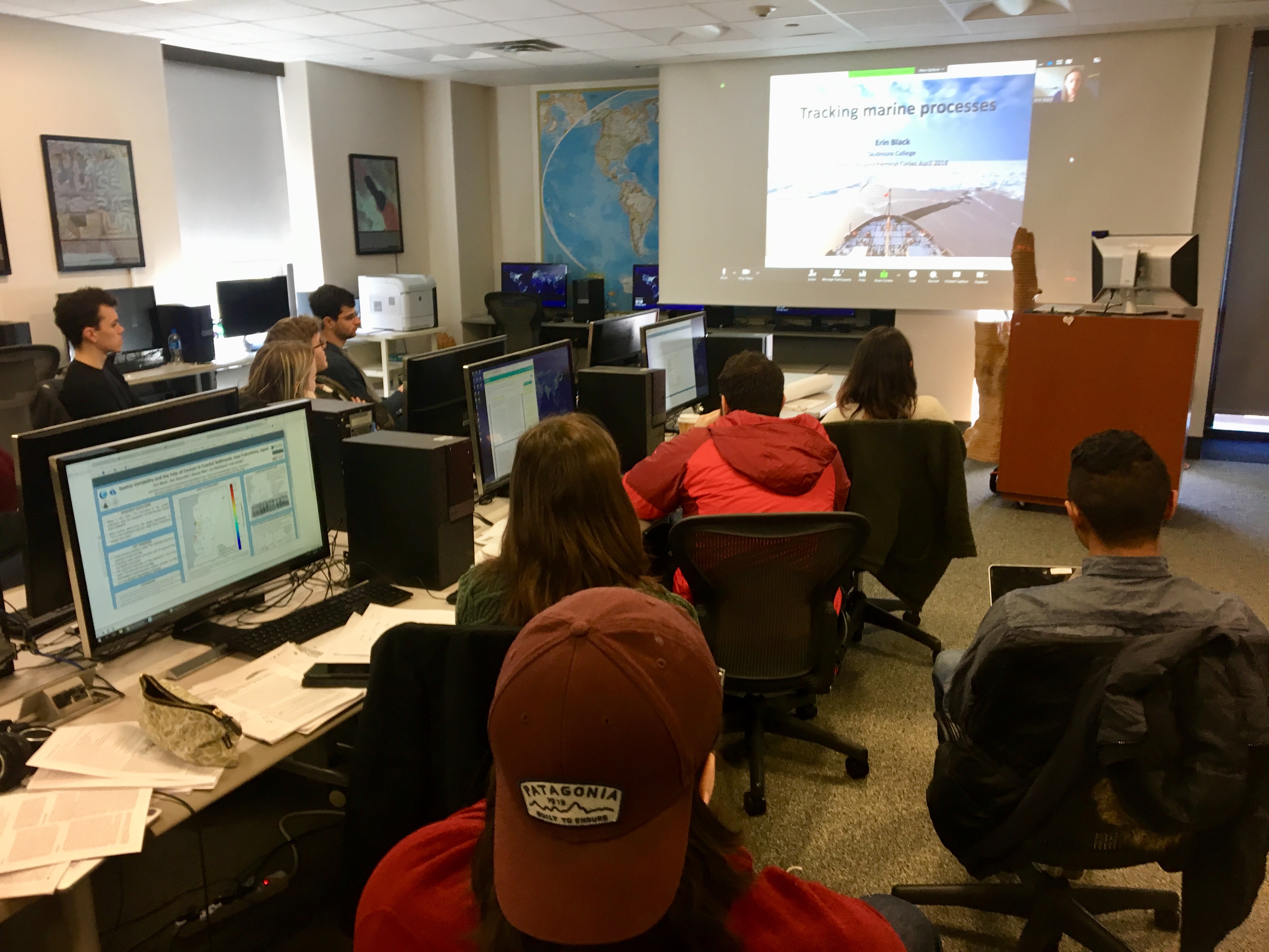 Students in the GIS center study a digital presentation while interacting on computers in the lab.