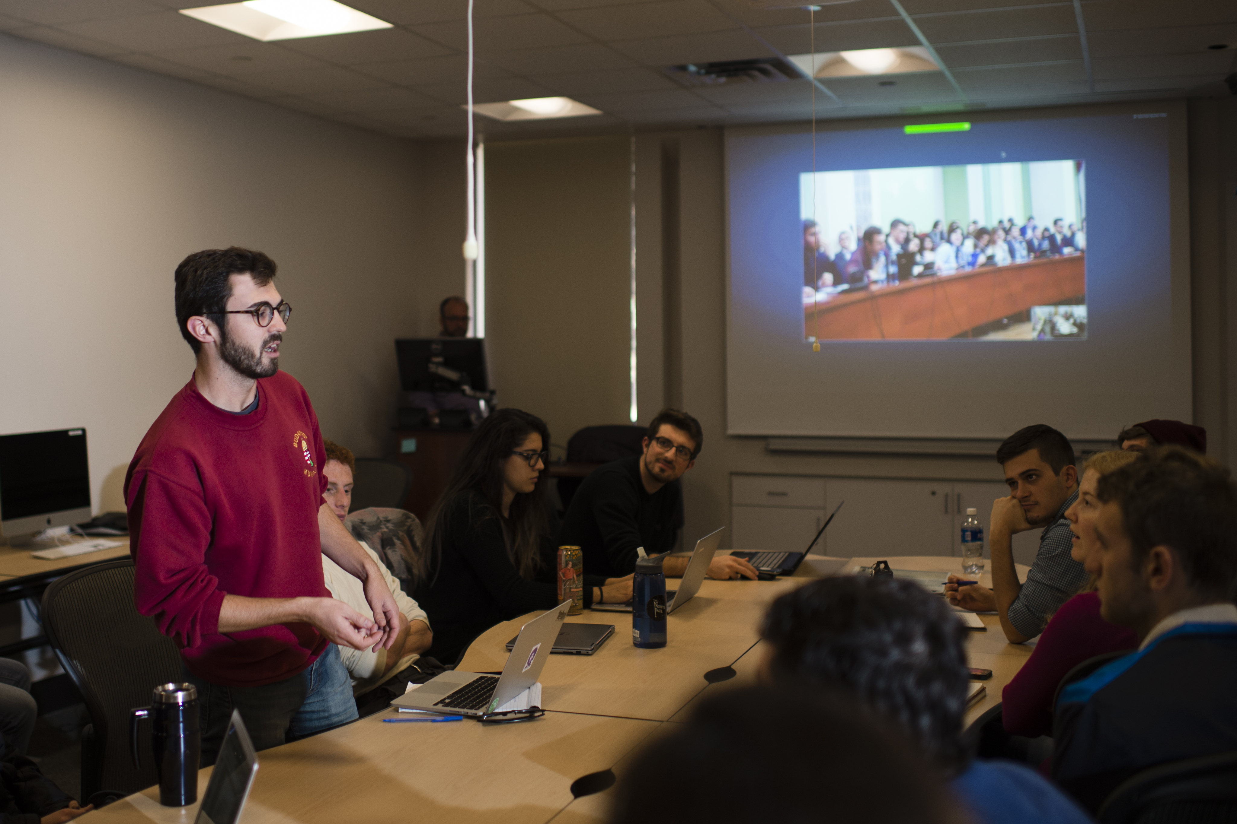 One student stands out from a group and speaks to panelists over video-communication in real time.