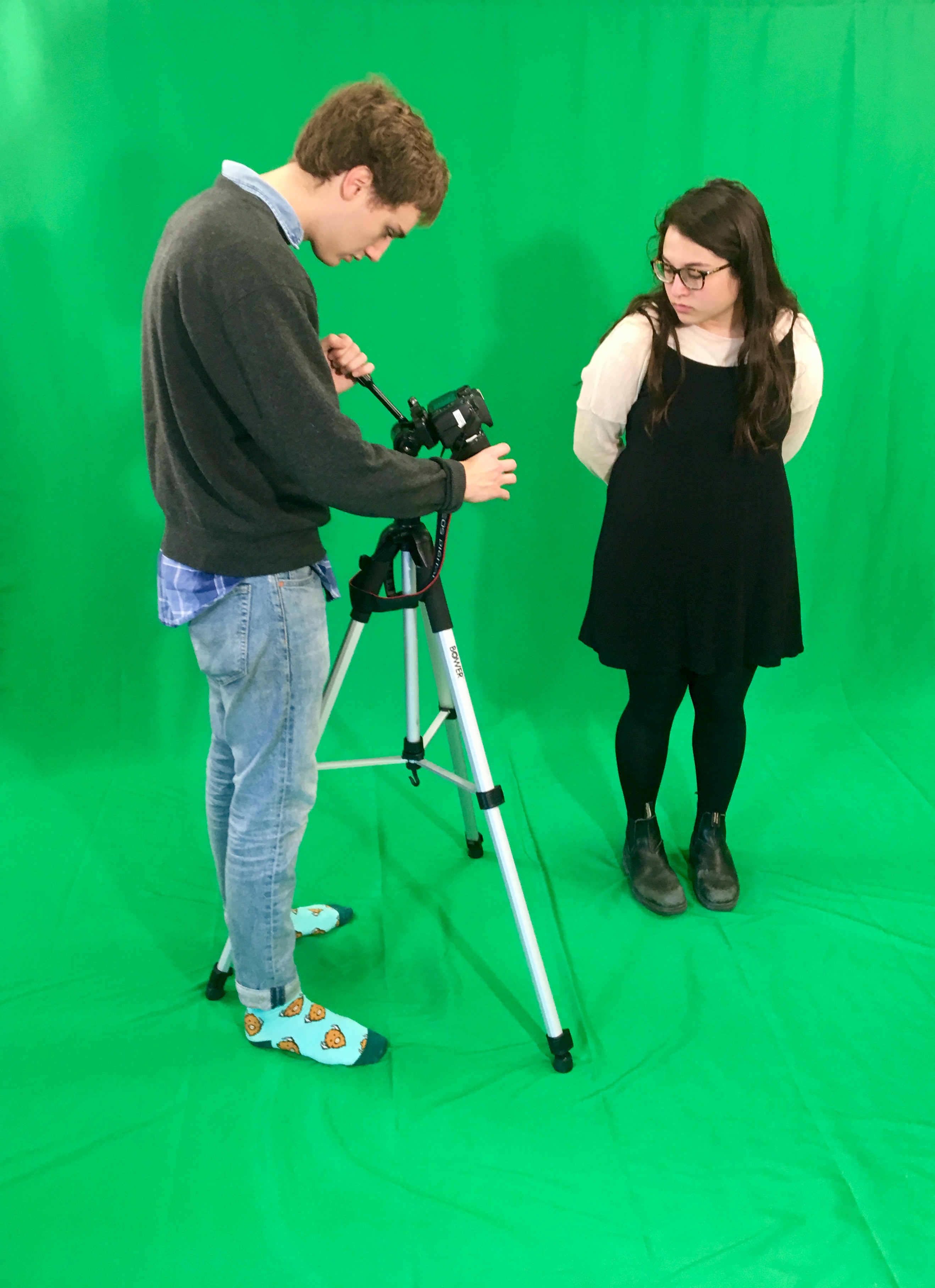 One student stands in front of a green screen while a LEDS assistant runs the camera.